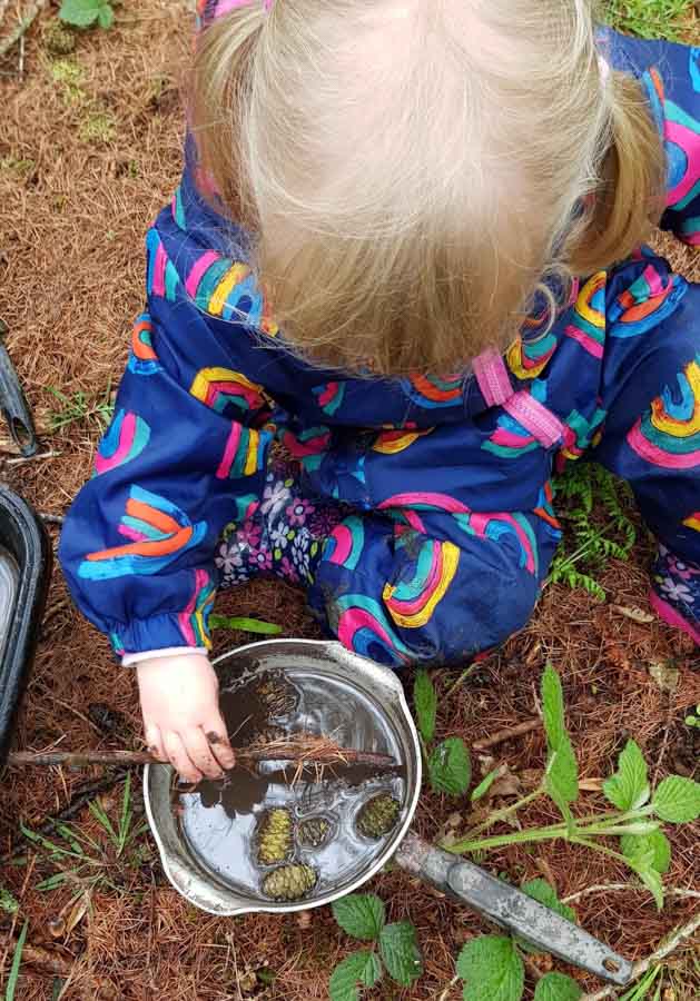 Child stiring muddy water in a pan with a stick outdorrs