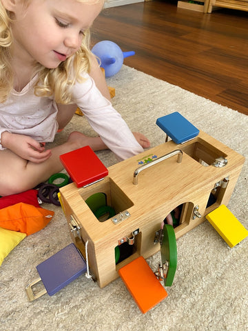 Little girl playing with a Montessori lock box quality wooden toy.