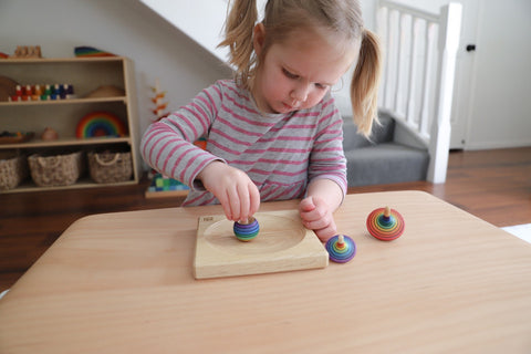 Little girl playing with Mater wooden spinning tops.