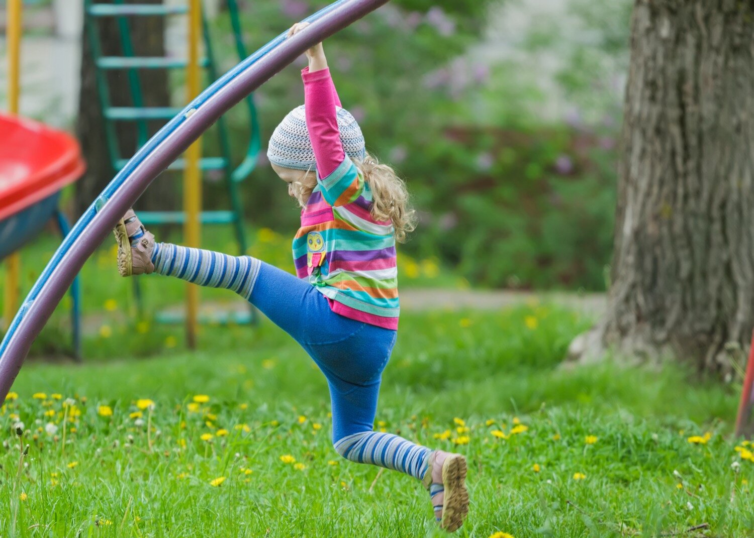 Young girl hanging from playground equipment. This obstacle courses is a movement games that can develop speech and language learning.