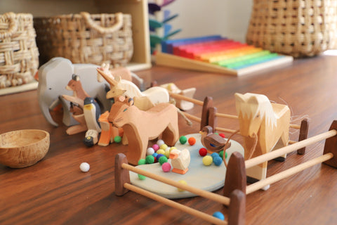 Wooden farm animal toys enclosed in a wooden toy fence.
