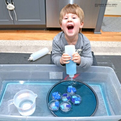 Toddler squirting blue water in a winter ice sensory bin.