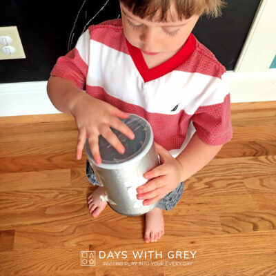 Preschooler shaking a homemade sound shaker to explore the sound it makes when shaken.