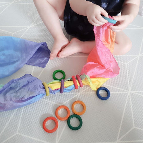 Little hands doing fine motor activity putting wooden toy rings onto a play silk.