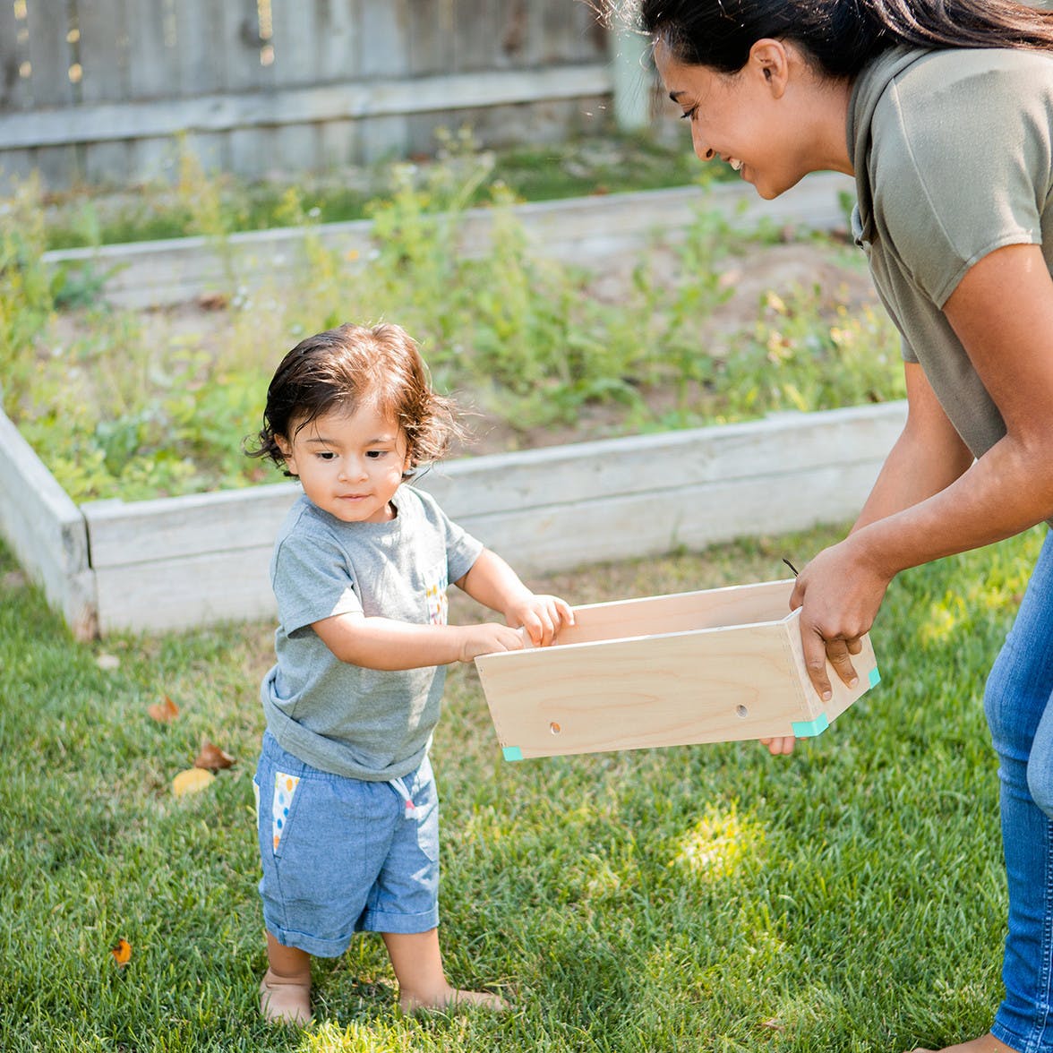 Woman and toddler carrying a wooden box together outside