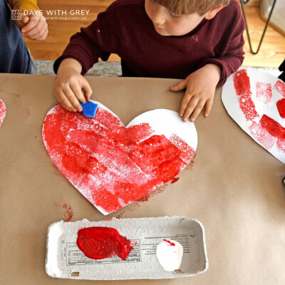 Preschooler painting a white heart with a sponge and red paint.