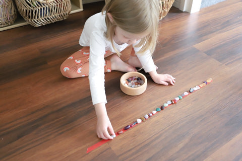 Little girl playing with crystals and washing tape, lining them up on the floor.