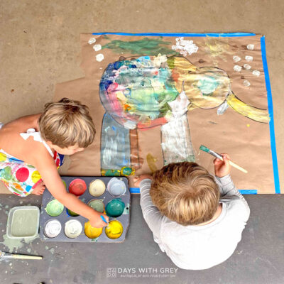Two boys are painting a large canvas of Elmer the Elephant.