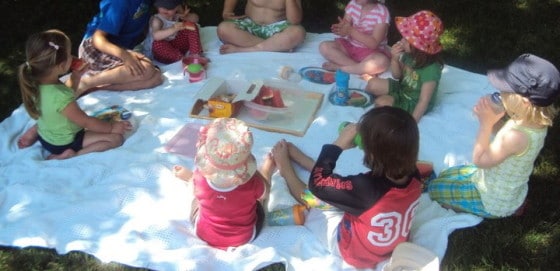 9 toddlers and preschoolers eating lunch on blanket in backyard