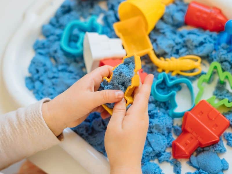 Image of a sensory bin with blue sand and a variety of different toys to play with in the sand. 