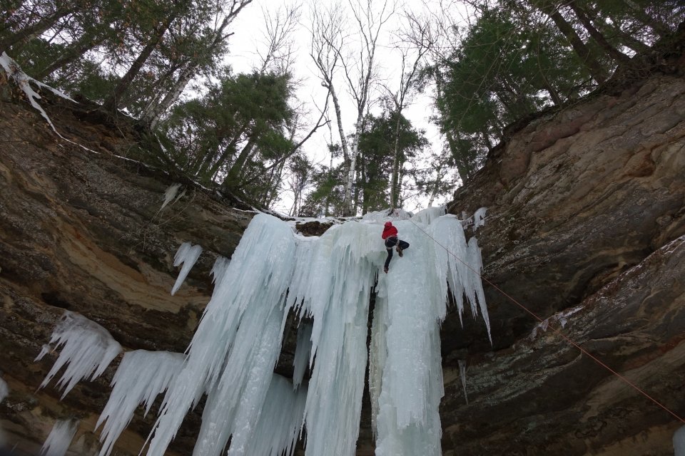 Ice climber near the top of a curtain and column of ice. The ice forms off and out of the sandstone rocks.