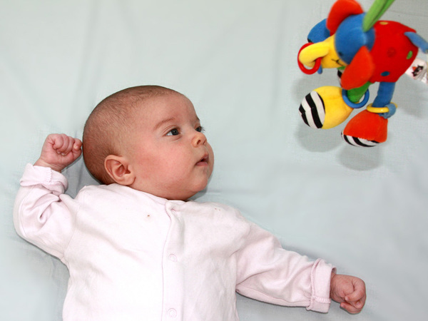 baby lying down fascinated by colourful toy