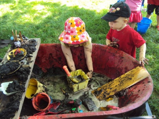 Kids playing with a wheelbarrow full of mud