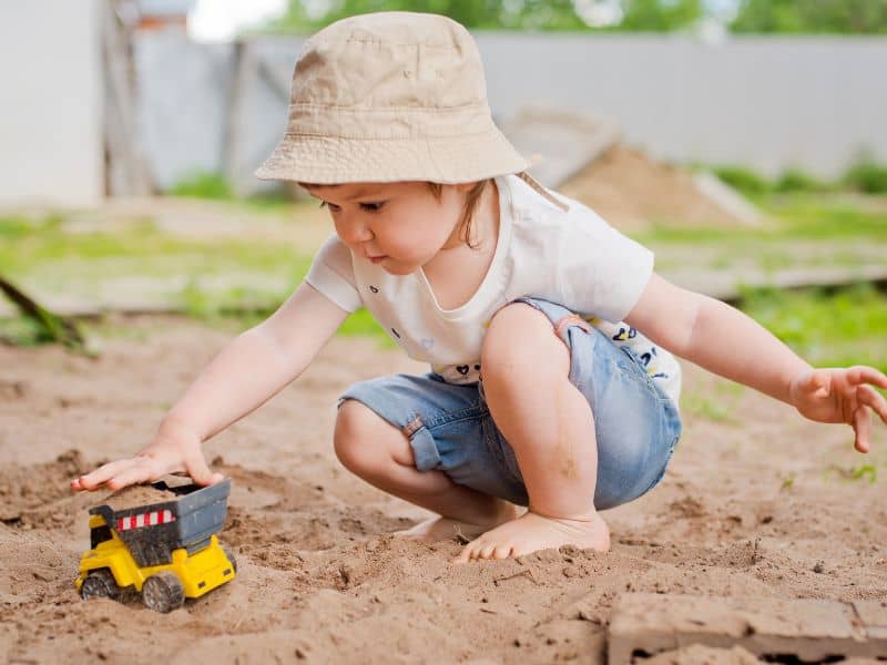 Child engaging in free play outside by driving a toy car through the sand. 