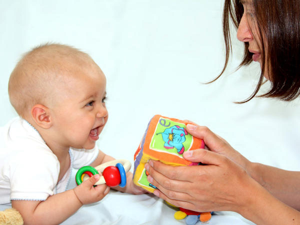 baby holding wooden toy and grabbing soft cube