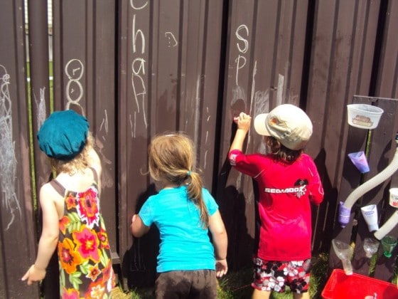 preschoolers drawing with chalk on brown metal fence