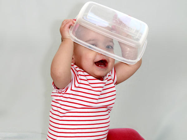 baby putting plastic container on her head