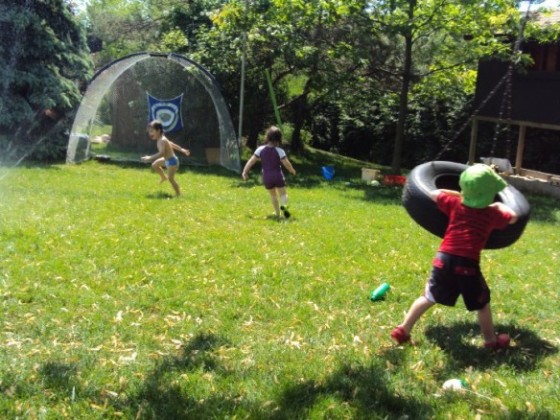 3 preschoolers running through sprinkler in backyard